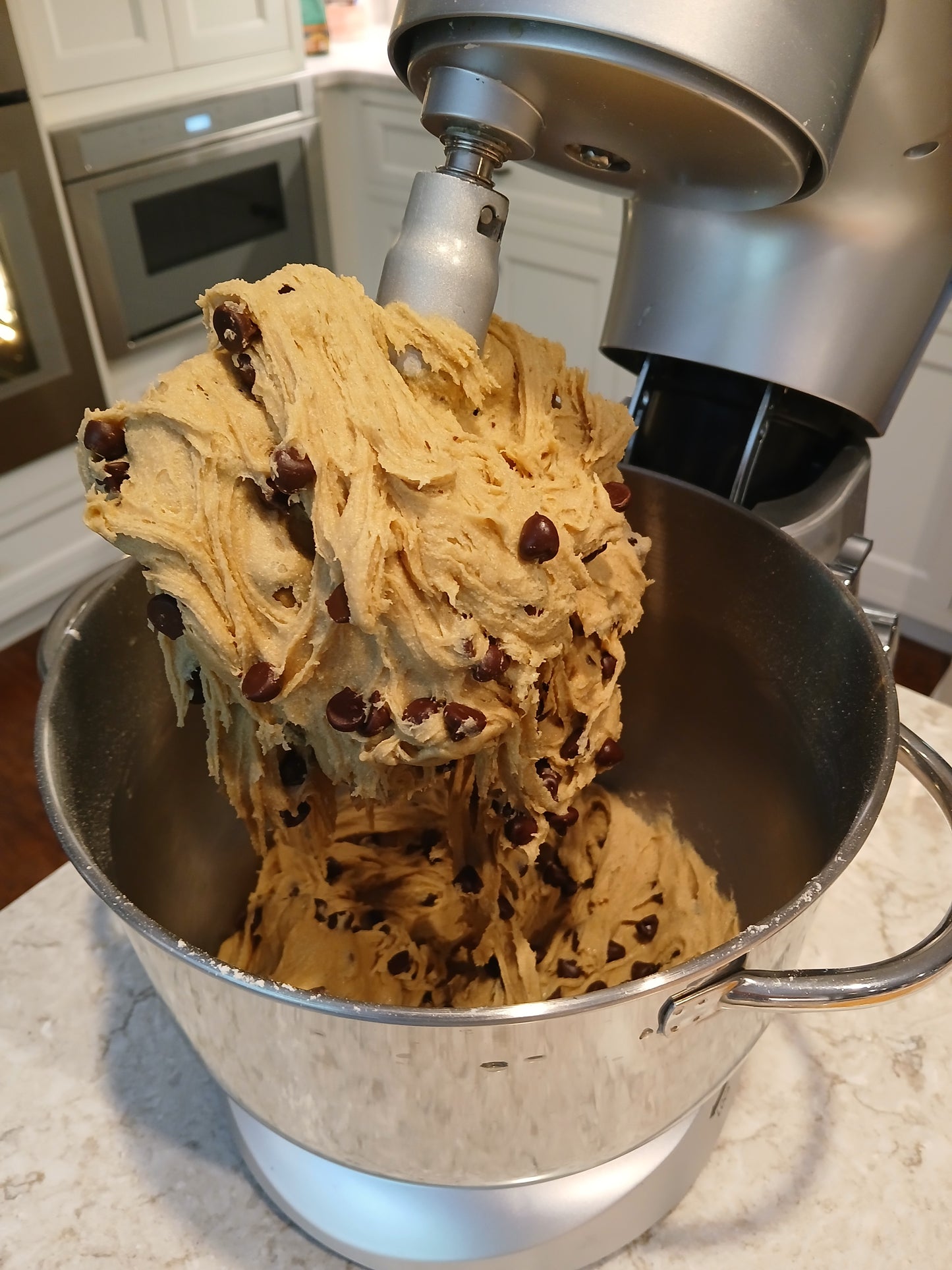 Bowl of cookie dough with chocolate chips being mixed by a stand mixer.