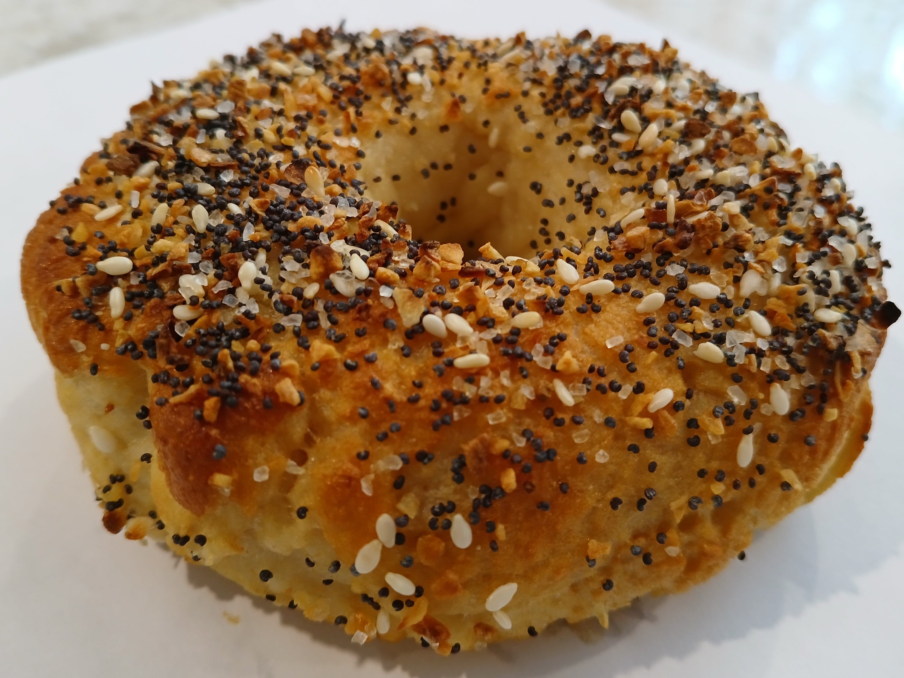 Bagel gluten free with everything seasoning on a white surface