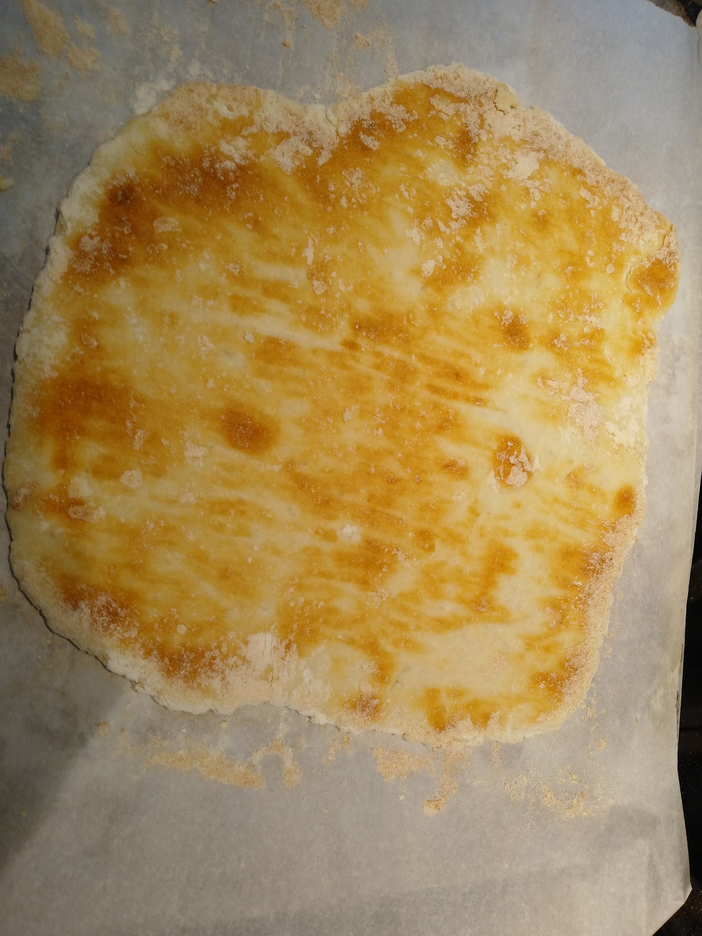 Baked gluten free pizza crust on a baking sheet with parchment paper