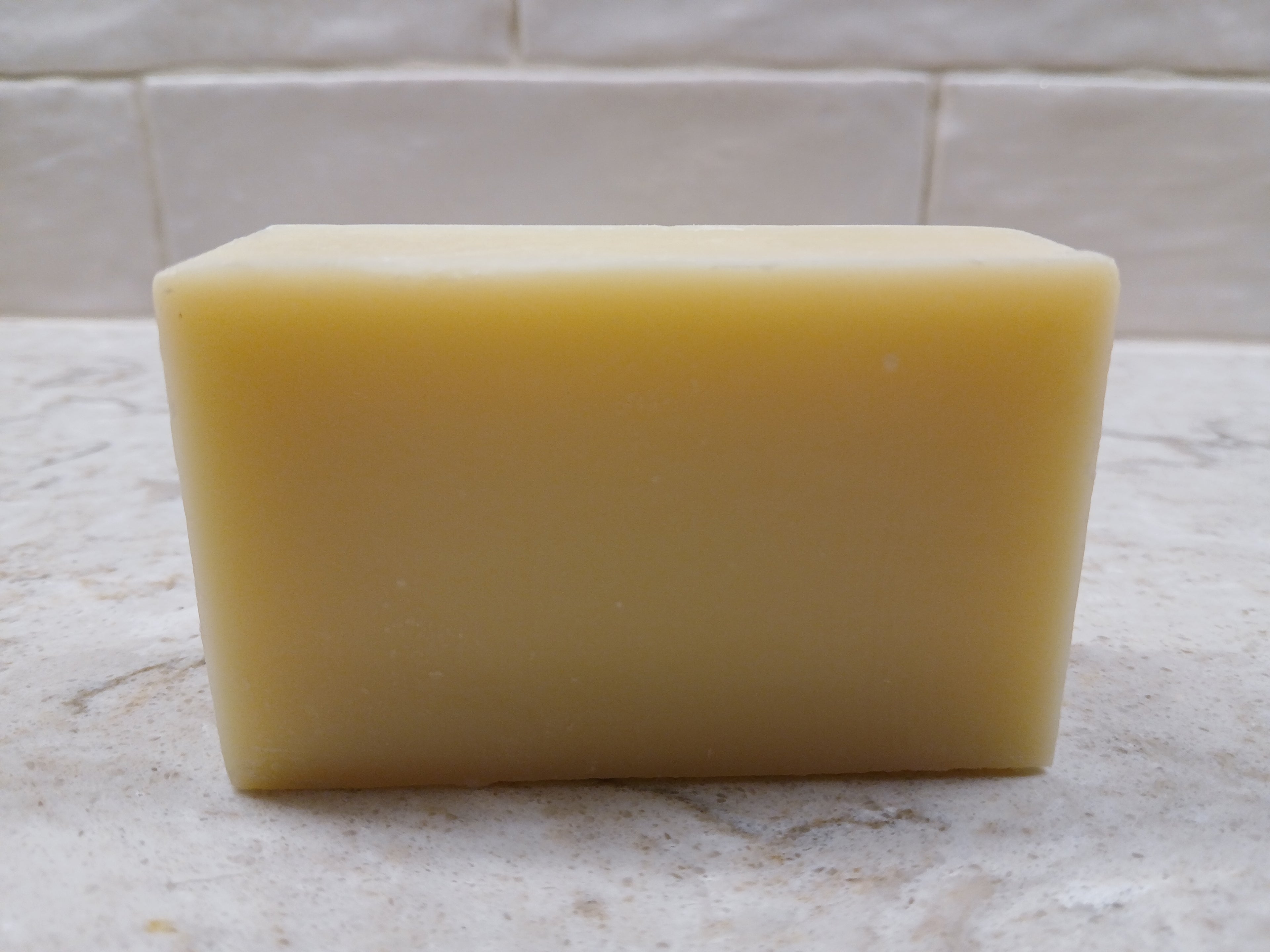 Yellow Lemongrass bar of soap on a marble surface with a tiled wall background