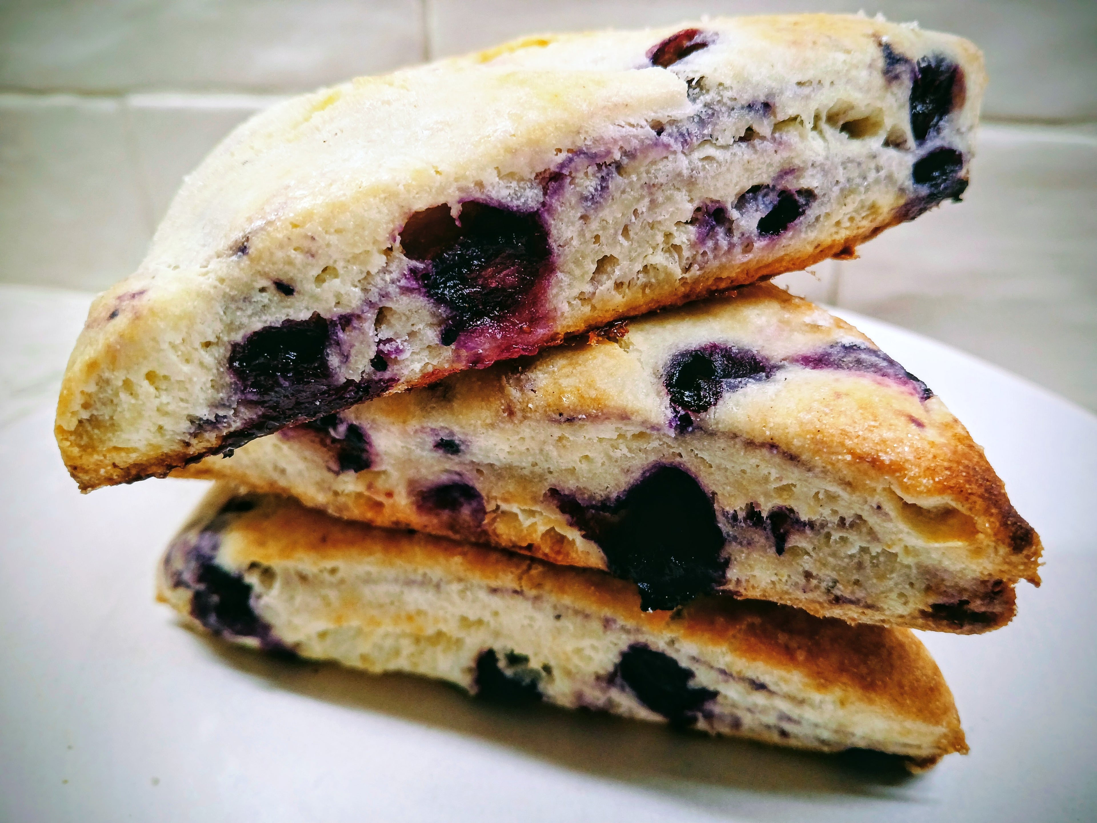 Three triangular GF blueberry scones stacked on a white plate with a tiled background.