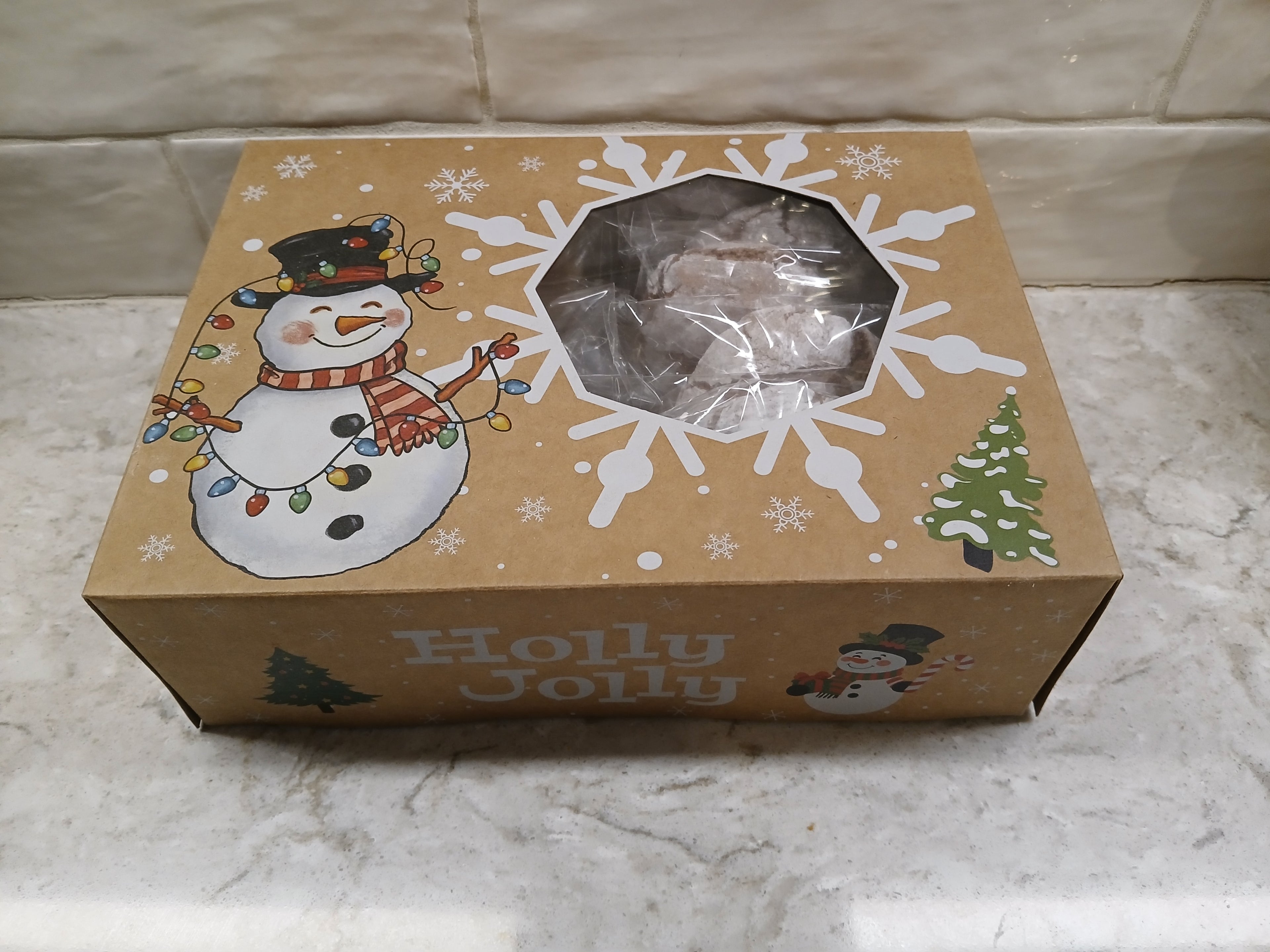 Box of gluten-free cookies with a snowman design and 'Holly Jolly' text on a marble surface