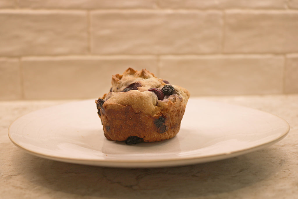 Blueberry muffin on a white plate with a beige tiled wall background