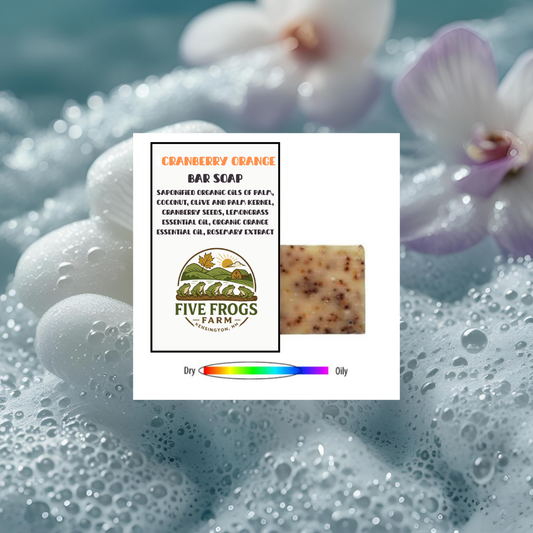 Five Frogs Farm cranberry orange bar soap with packaging on a wet surface with flowers in the background