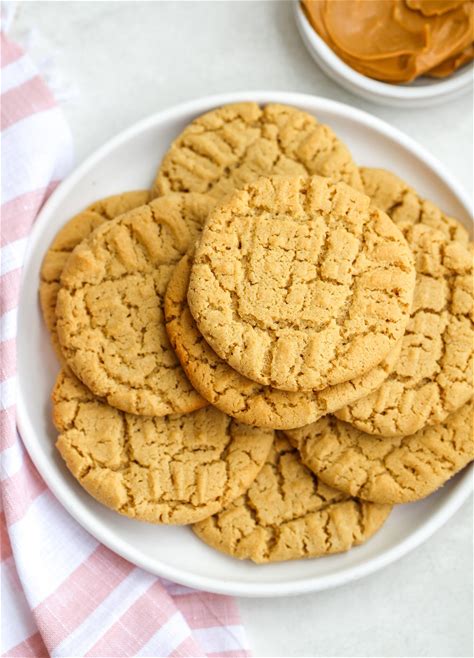 Stack of peanut butter cookies on a white plate with a bowl of peanut butter in the background.