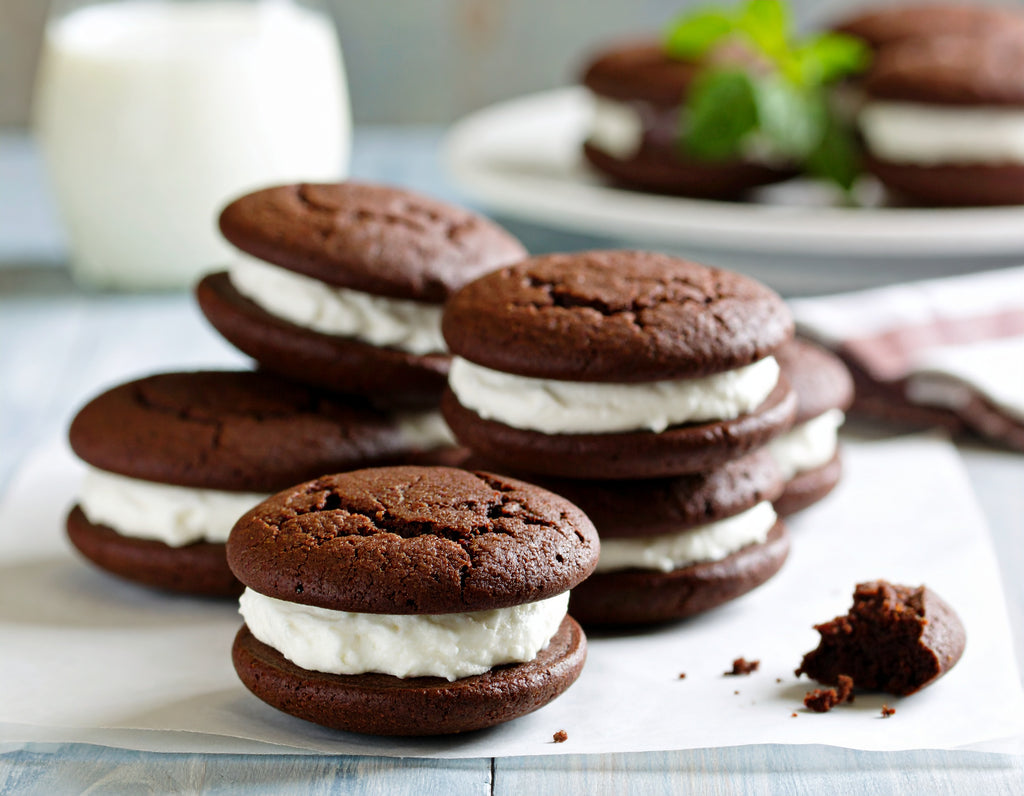 Stack of chocolate whoopie pies with cream filling on a white surface.
