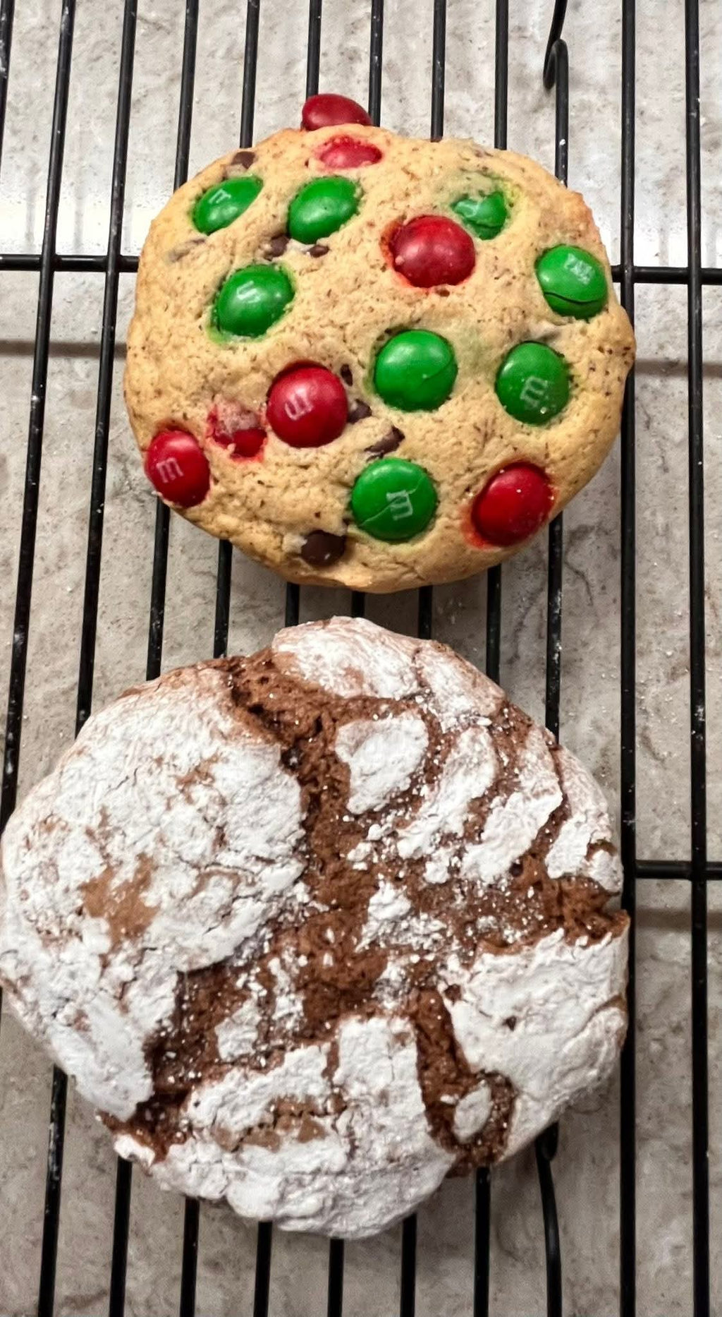 Two gluten-free cookies on a cooling rack, one chocolate crinkle cookie with powdered sugar and the other M&M cookie.